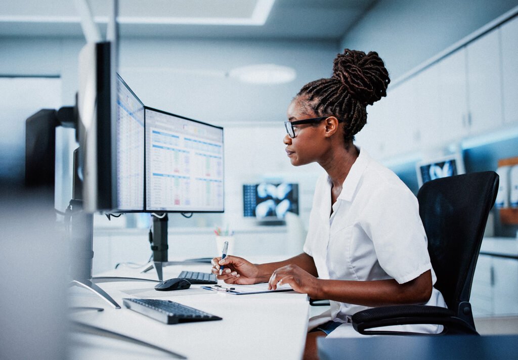 A woman in scrubs reviews information on a computer screen.