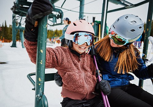 A woman and young girl sit together on a ski lift chair.