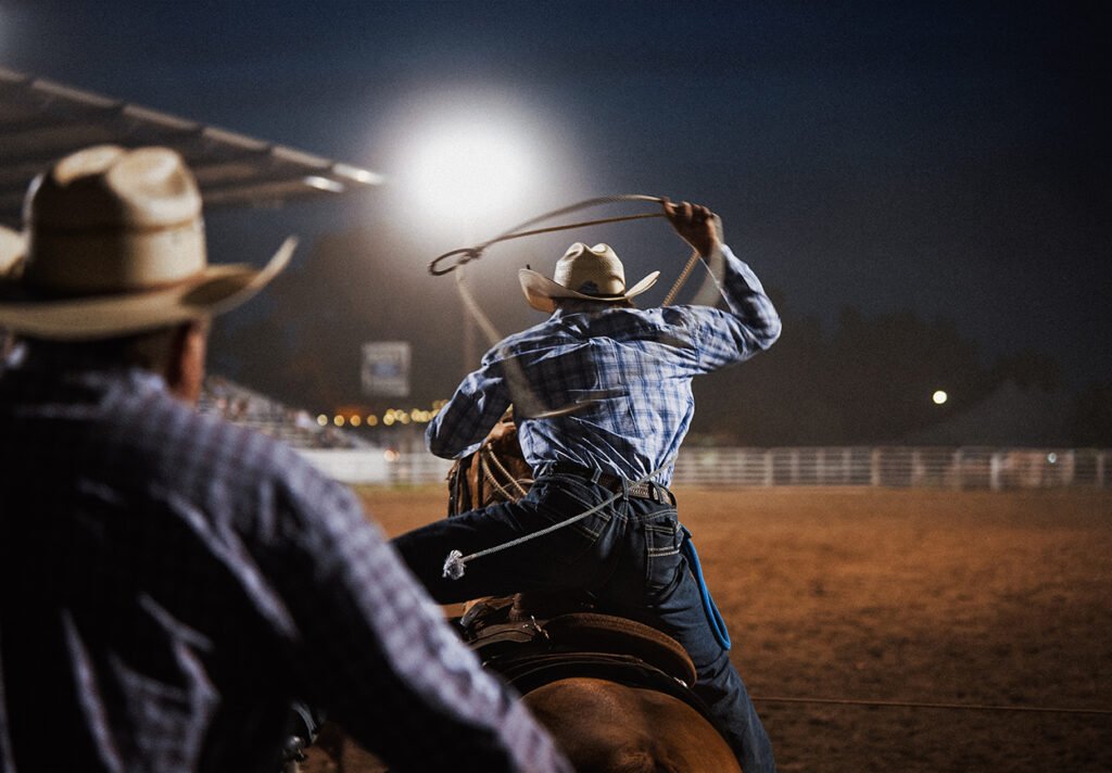A cowboy swings his lasso above his head while on horseback.