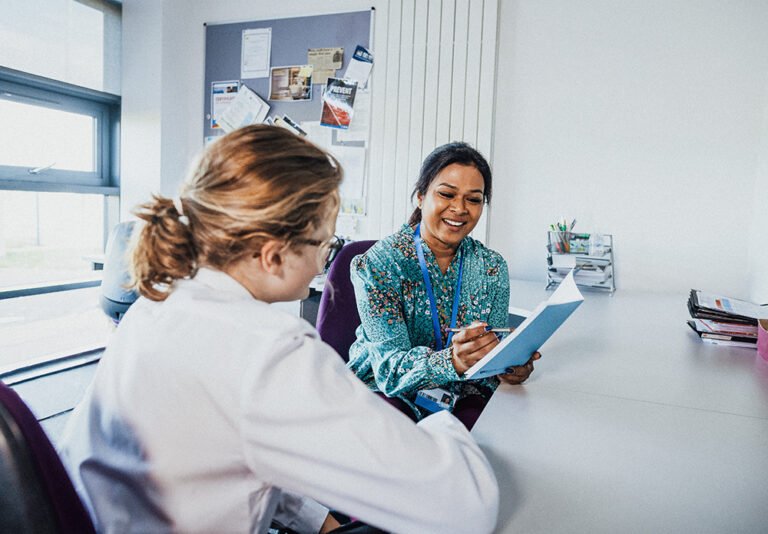 Two women review paperwork at a desk.