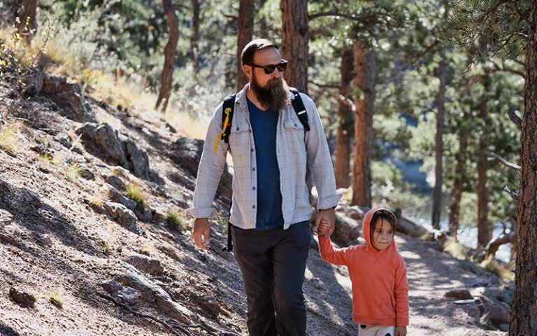 A man holds hands with a young girl on an outdoor trail.