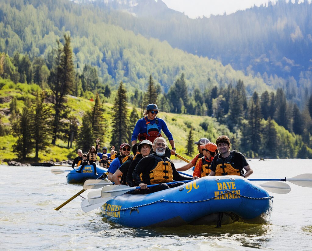 A group of men and women, dressed in life jackets, sit in inflatable rafts on the water.